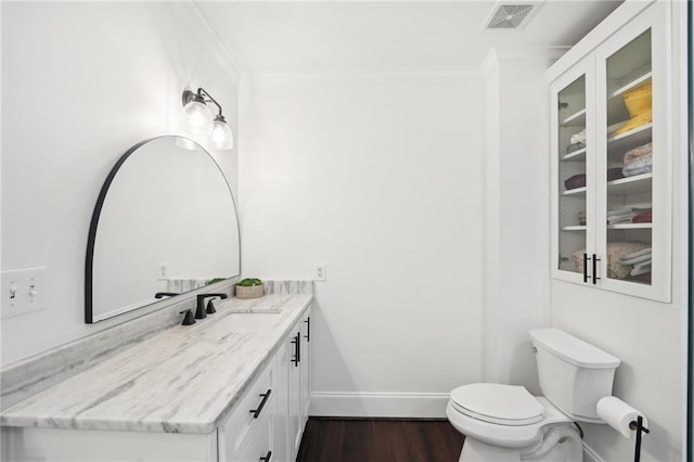 half bathroom with toilet, visible vents, wood finished floors, vanity, and ornamental molding