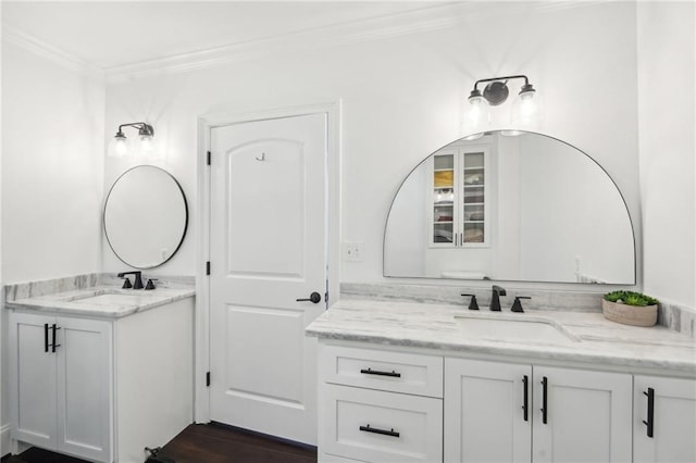 bathroom featuring two vanities, wood finished floors, ornamental molding, and a sink