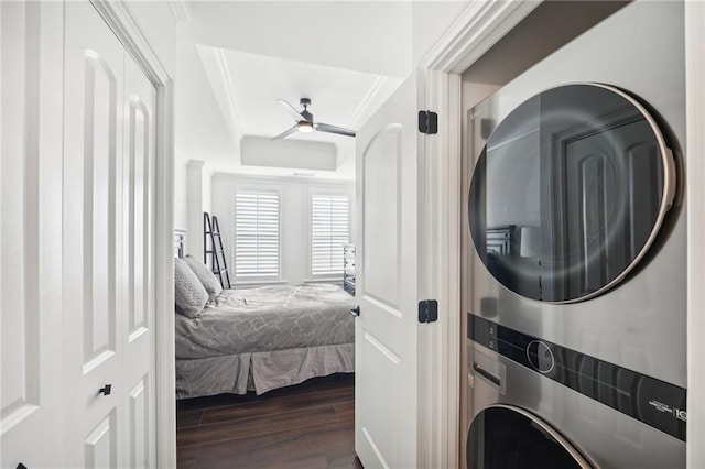 laundry room featuring dark wood-style flooring, a ceiling fan, crown molding, stacked washing maching and dryer, and laundry area