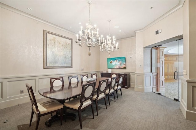 dining area with a wainscoted wall, ornamental molding, light carpet, a decorative wall, and a chandelier