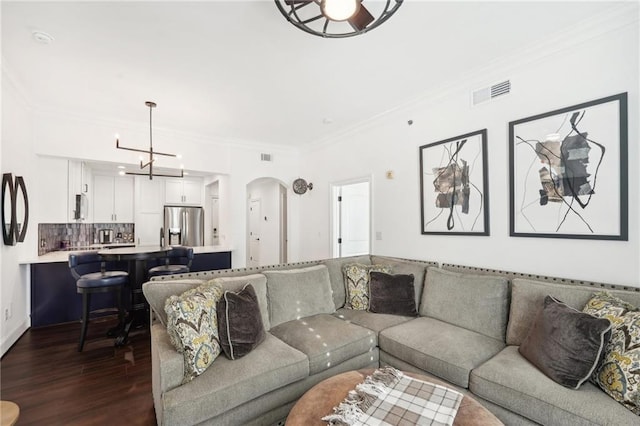living area featuring dark wood finished floors, an inviting chandelier, visible vents, arched walkways, and crown molding