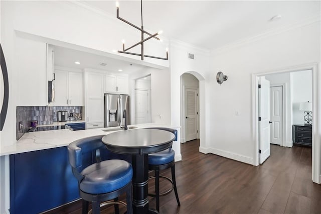 kitchen featuring white cabinets, a peninsula, arched walkways, stainless steel fridge, and backsplash