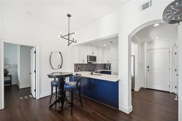 kitchen with white cabinets, stainless steel microwave, visible vents, decorative backsplash, and crown molding