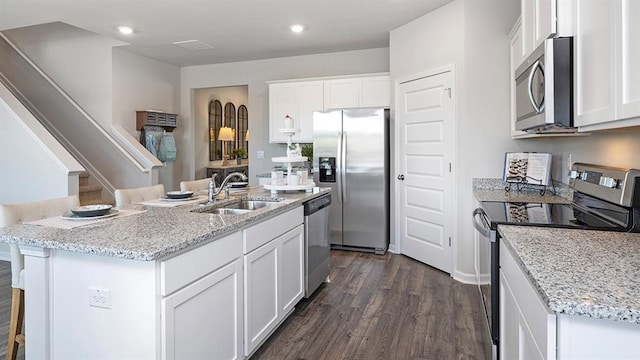 kitchen featuring dark wood-style floors, stainless steel appliances, white cabinets, a sink, and light stone countertops