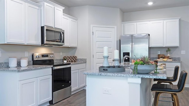 kitchen with a kitchen island with sink, a breakfast bar, white cabinetry, appliances with stainless steel finishes, and dark wood finished floors