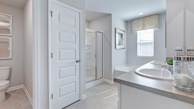 bathroom with double vanity, toilet, a stall shower, a sink, and baseboards