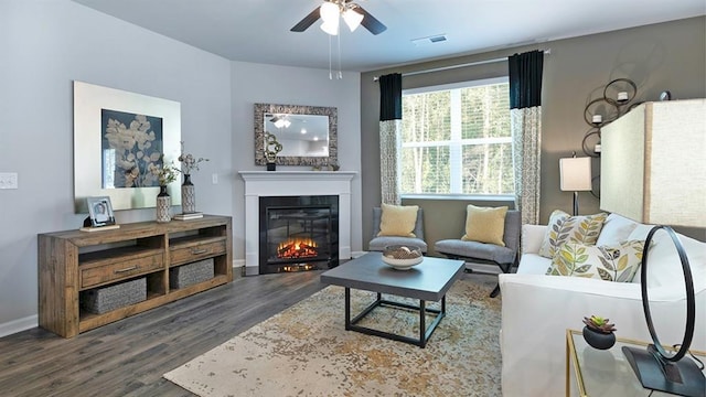 living room featuring baseboards, visible vents, a ceiling fan, a glass covered fireplace, and wood finished floors