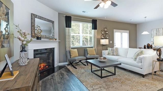 living area featuring a glass covered fireplace, visible vents, ceiling fan, and wood finished floors