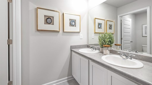 full bathroom featuring baseboards, a sink, toilet, and double vanity