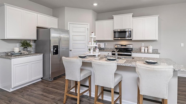 kitchen with white cabinetry, a kitchen bar, appliances with stainless steel finishes, and dark wood-style flooring