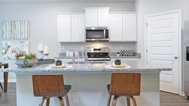 kitchen with a kitchen island with sink, wood finished floors, white cabinetry, a kitchen breakfast bar, and appliances with stainless steel finishes