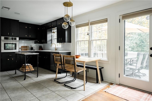 kitchen with a wealth of natural light, hanging light fixtures, stainless steel oven, and backsplash