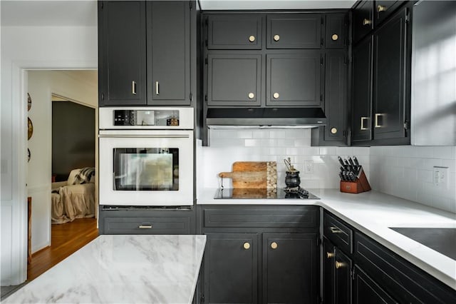 kitchen featuring cooktop, hardwood / wood-style flooring, oven, and decorative backsplash