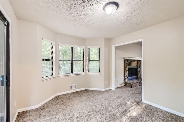 carpeted empty room with a textured ceiling and a fireplace