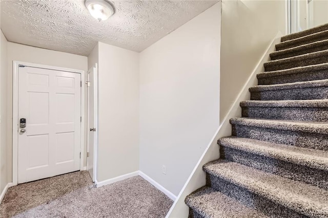 stairway with a textured ceiling and carpet floors