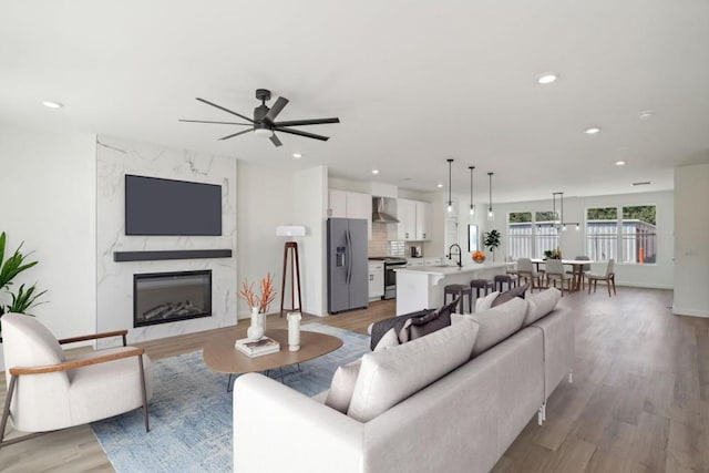 living room with ceiling fan, sink, light wood-type flooring, and a high end fireplace