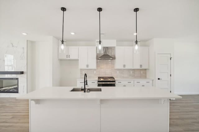 kitchen featuring wall chimney range hood, a center island with sink, and stainless steel range oven