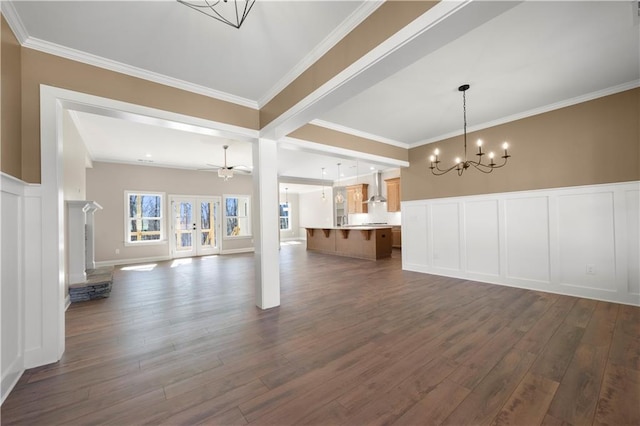 unfurnished living room with ornamental molding, dark wood-style flooring, a decorative wall, and ceiling fan with notable chandelier