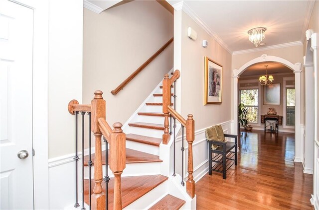 stairway with ornate columns, ornamental molding, wood-type flooring, and a notable chandelier