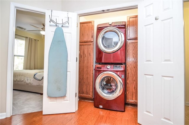 laundry room with light wood-type flooring, cabinets, ceiling fan, and stacked washer / dryer