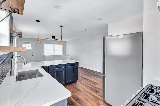 kitchen featuring a sink, a ceiling fan, freestanding refrigerator, light stone countertops, and wood finished floors