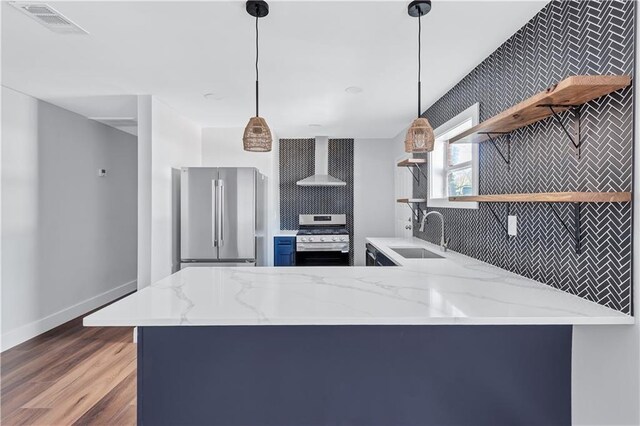 kitchen featuring open shelves, stainless steel appliances, a sink, wall chimney range hood, and a peninsula