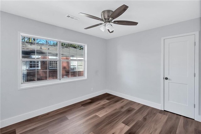 empty room featuring a ceiling fan, dark wood-type flooring, baseboards, and visible vents