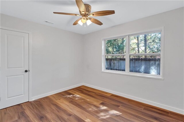 unfurnished room with a ceiling fan, visible vents, baseboards, and wood finished floors