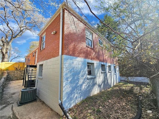 view of side of home featuring fence, central AC, and stairway