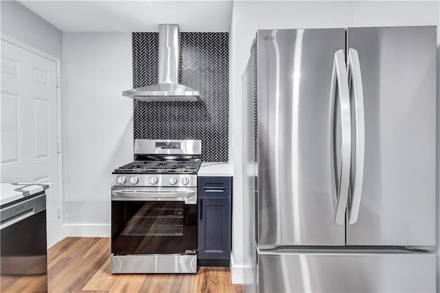 kitchen featuring light countertops, stainless steel appliances, decorative backsplash, wall chimney range hood, and light wood-style flooring