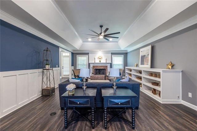3845 Glen Ian Dr, Loganville, GA 30052 - living room with ceiling fan, a brick fireplace, a tray ceiling, dark wood-style flooring, and ornamental molding