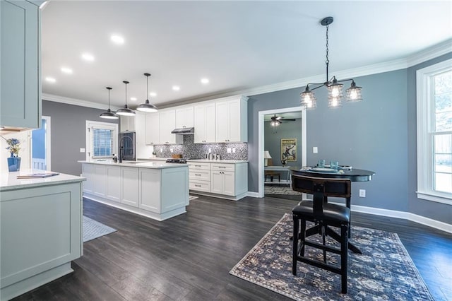 3845 Glen Ian Dr, Loganville, GA 30052 - kitchen featuring decorative backsplash, under cabinet range hood, a kitchen island with sink, healthy amount of natural light, and ornamental molding