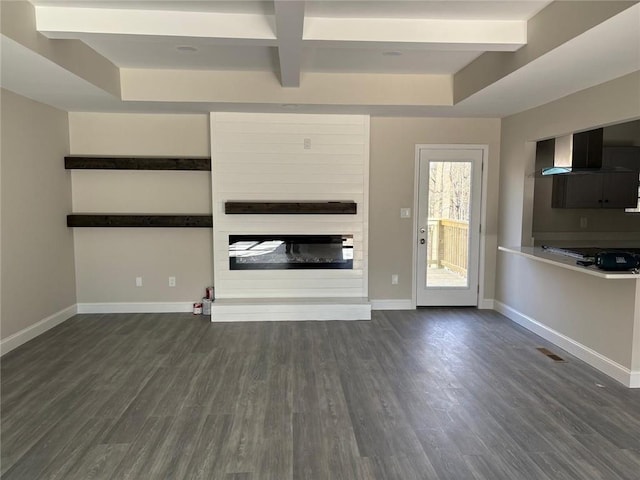 unfurnished living room featuring a large fireplace, beamed ceiling, dark wood finished floors, and baseboards