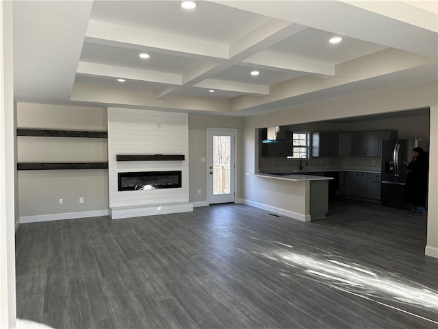 unfurnished living room with beam ceiling, dark wood-style flooring, a large fireplace, and baseboards