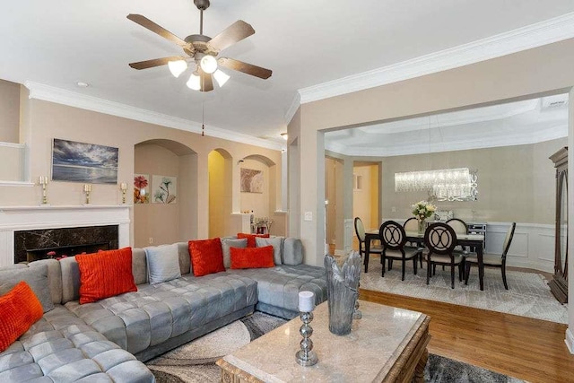 living room featuring ceiling fan with notable chandelier, wood-type flooring, ornamental molding, and a premium fireplace