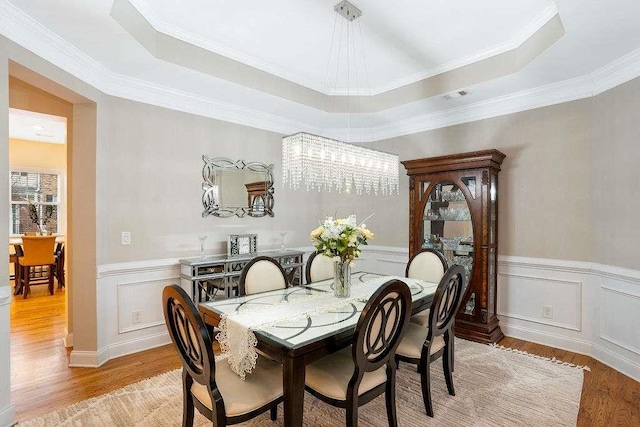 dining room featuring ornamental molding, a tray ceiling, and light hardwood / wood-style flooring