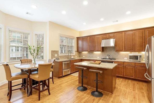 kitchen featuring sink, appliances with stainless steel finishes, light stone counters, a kitchen island, and light wood-type flooring