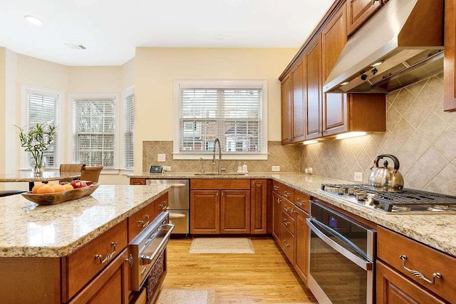 kitchen featuring stainless steel appliances, light stone countertops, sink, and exhaust hood