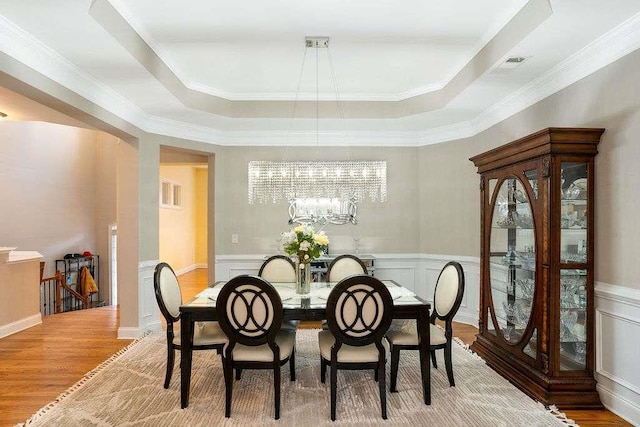 dining space featuring crown molding, wood-type flooring, a tray ceiling, and a chandelier