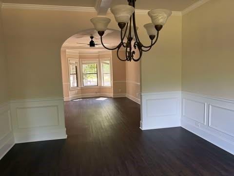 1307 Clarecastle Ln, Buford, GA 30519 - unfurnished dining area featuring a chandelier, arched walkways, dark wood-style flooring, crown molding, and a wainscoted wall