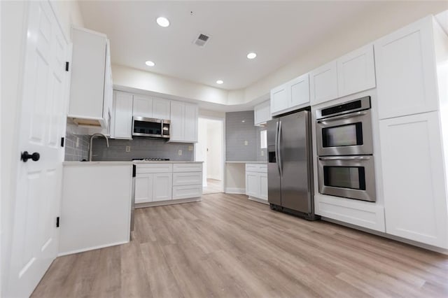 kitchen featuring white cabinets, appliances with stainless steel finishes, backsplash, and light hardwood / wood-style flooring