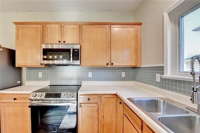 kitchen featuring stainless steel appliances, light countertops, backsplash, light brown cabinets, and a sink