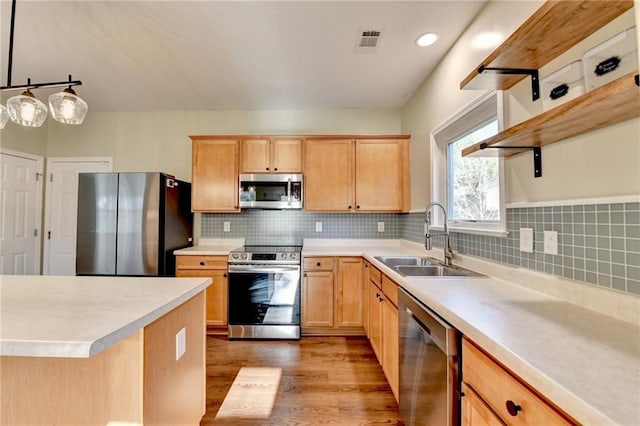 kitchen with pendant lighting, light countertops, backsplash, appliances with stainless steel finishes, and a sink