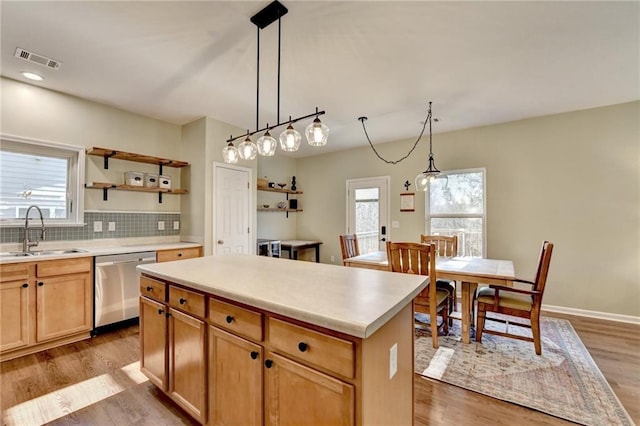 kitchen featuring stainless steel dishwasher, light countertops, a sink, and a center island