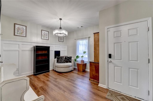 entrance foyer featuring light wood-style flooring, visible vents, a decorative wall, and a notable chandelier