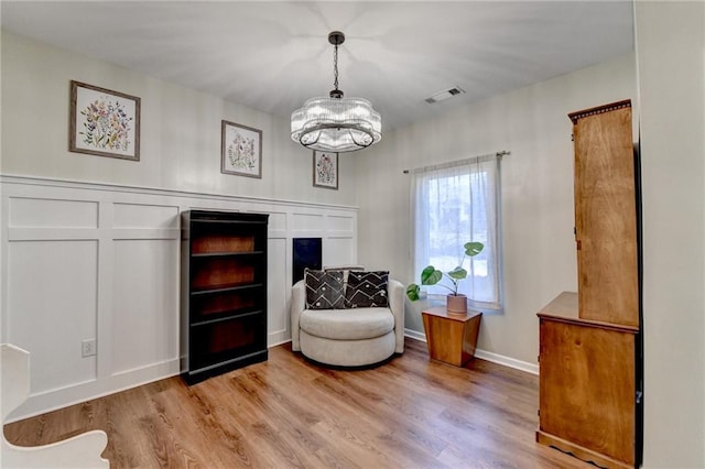 living area with a decorative wall, wood finished floors, visible vents, and a notable chandelier