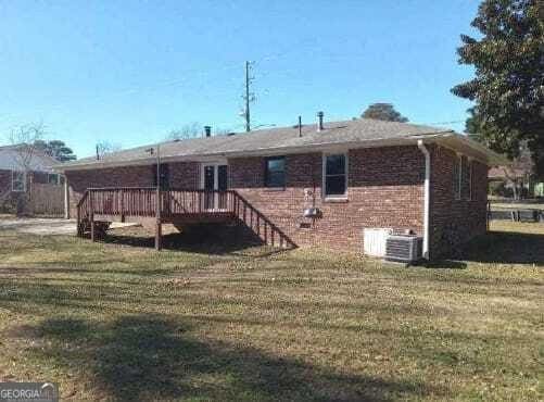 rear view of house featuring a lawn, brick siding, and a wooden deck