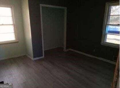 unfurnished bedroom with multiple windows, wood finished floors, a closet, and baseboards