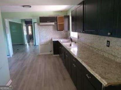 kitchen with baseboards, light countertops, dark cabinetry, light wood-style floors, and a sink