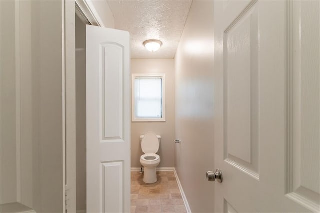 bathroom featuring toilet, a textured ceiling, and baseboards